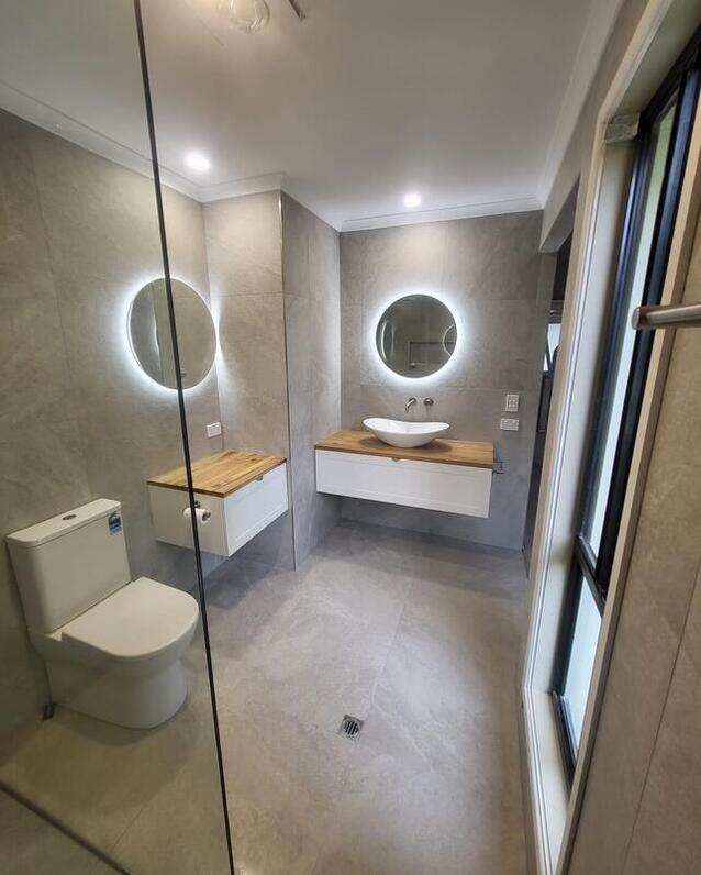 bathroom with a toilet and a sink with two circular mirrors on the walls with lights behind them